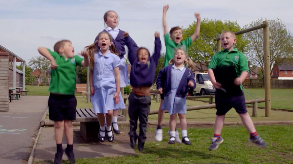 Children in school uniforms jumping and celebrating outdoors in a park. ESG Video