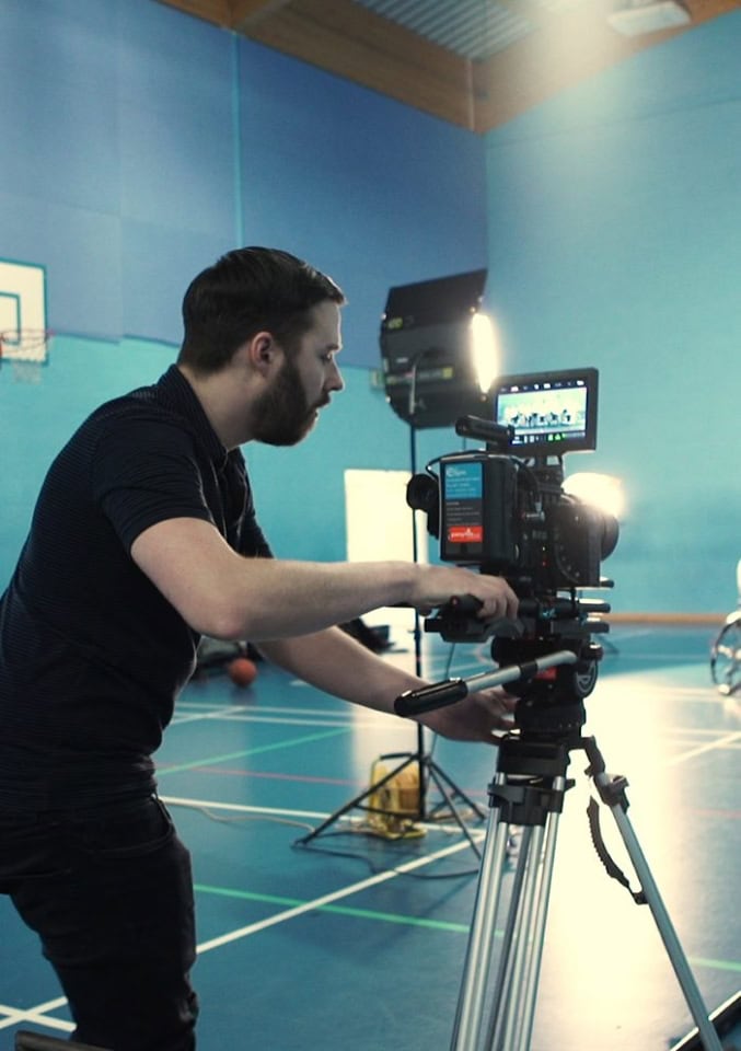 Cinematic filmmaker filming in sports hall for documentary or promotional video.