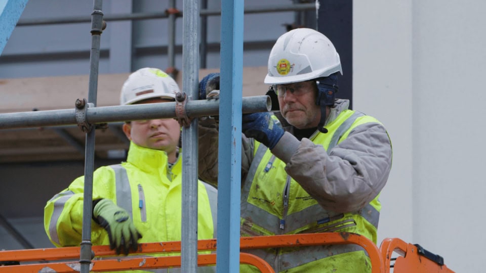 Construction workers inspecting scaffolding at a building site for documentary footage.