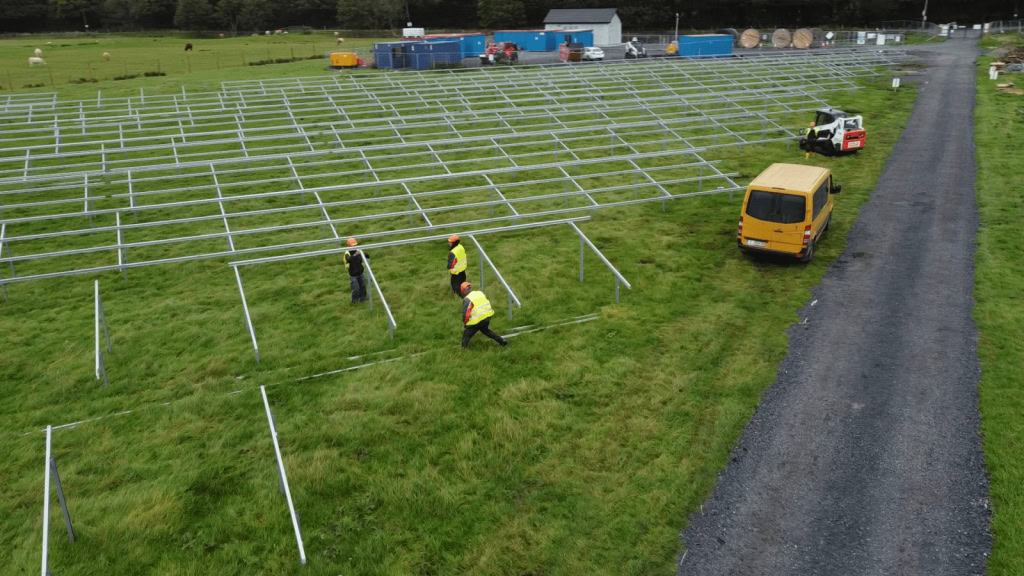 Solar panel installation on a green field with workers in safety gear installing photovoltaic structures.