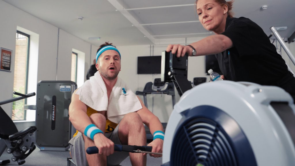 Gym workout with a man on a rowing machine in a modern fitness centre. Fresh video content.