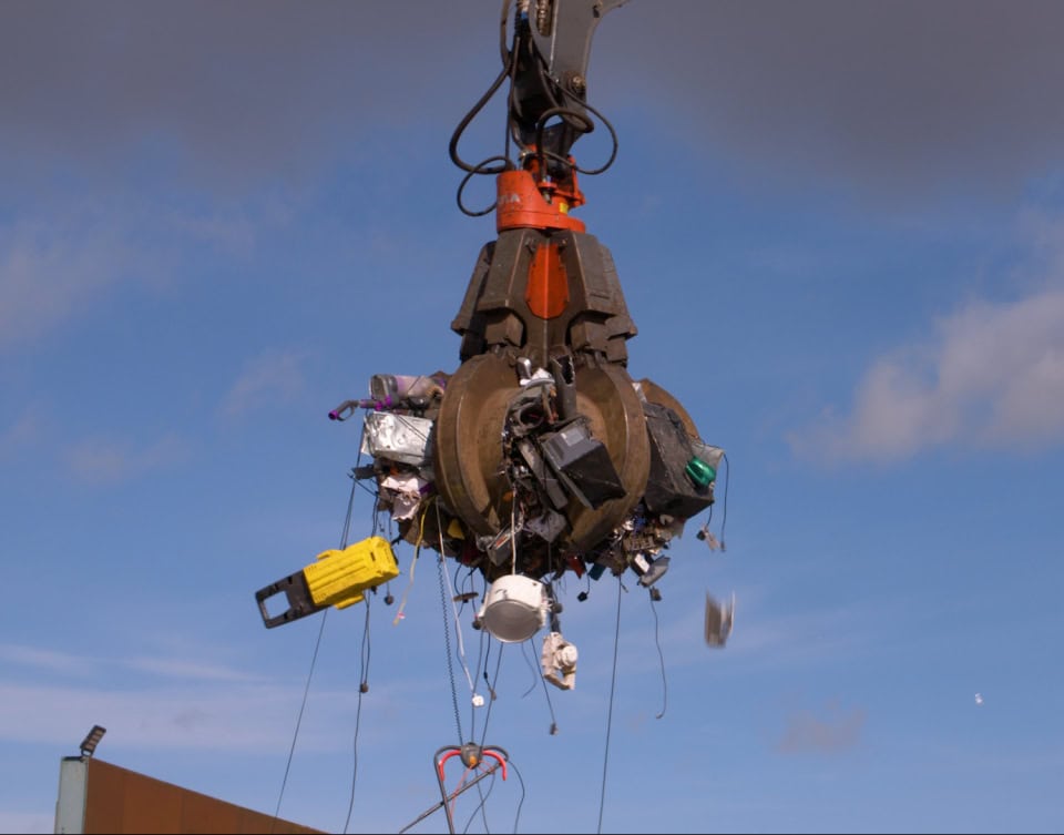 Gigantic robot claw lifting debris against a blue sky.