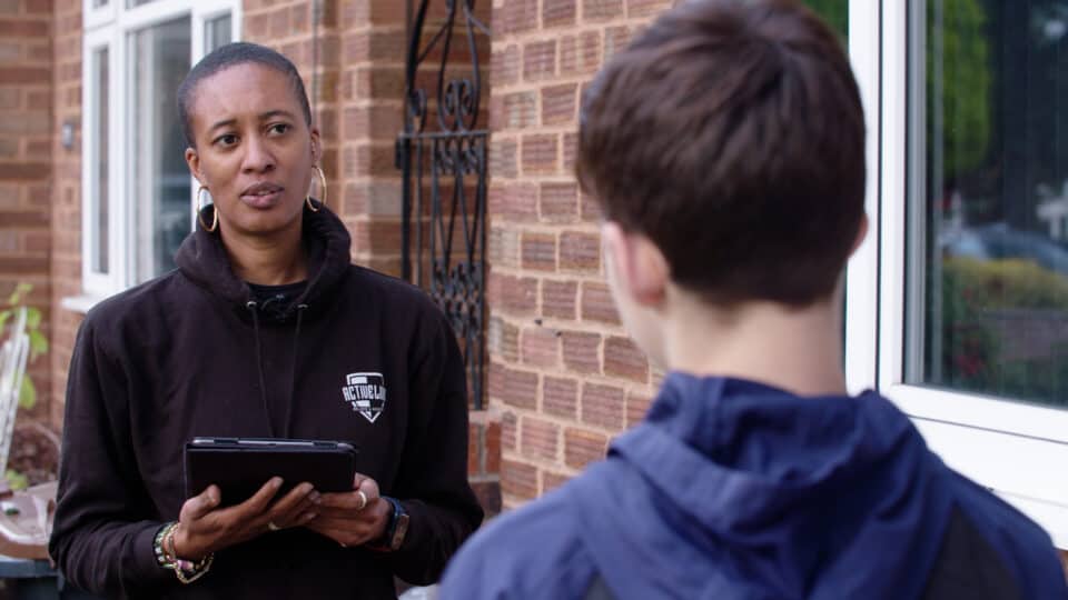 Entrepreneurship interview outside house, woman speaking to a young man, discussing business opportunities, outdoor setting, real estate, community engagement.