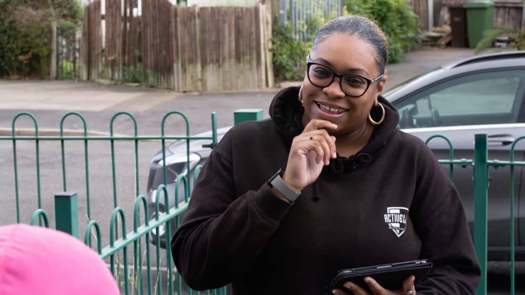 Feminist woman smiling outdoors, holding a tablet, wearing glasses and a hoodie, urban setting.