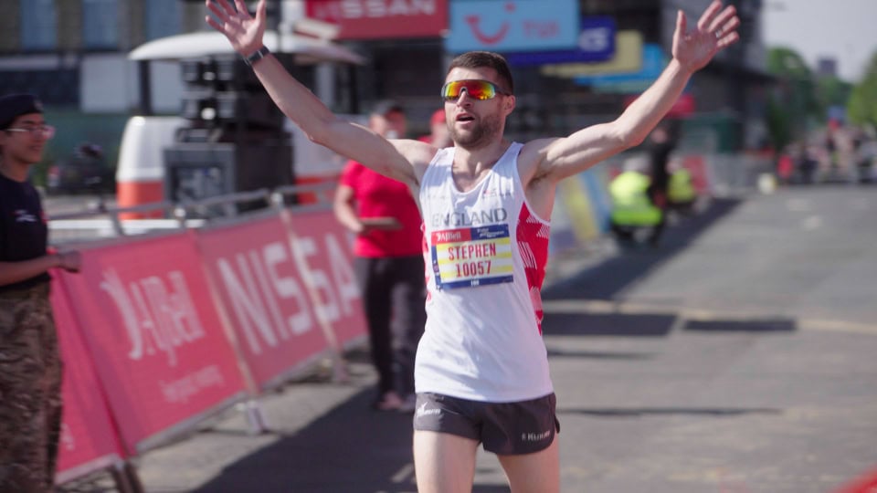 Elite male marathon runner crossing finish line with arms raised, urban race event, athlete in sportswear.