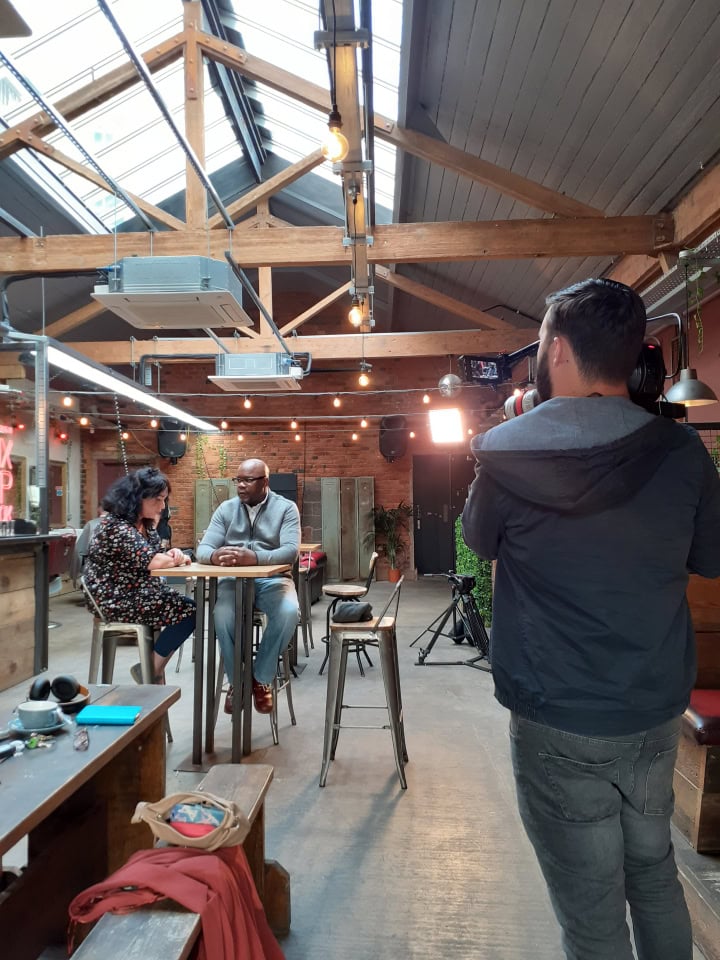 Behind-the-scenes filming of an interview inside a modern, stylish cafe with professional lighting and camera setup.