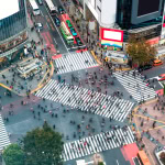 Busy city intersection with pedestrians, cars, and tall modern buildings in Tokyo, Japan at dusk.