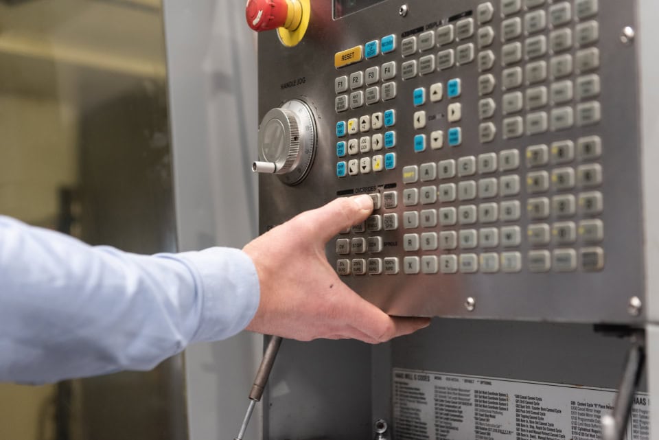 A machine operator adjusting a CNC machine control panel in a manufacturing setting.