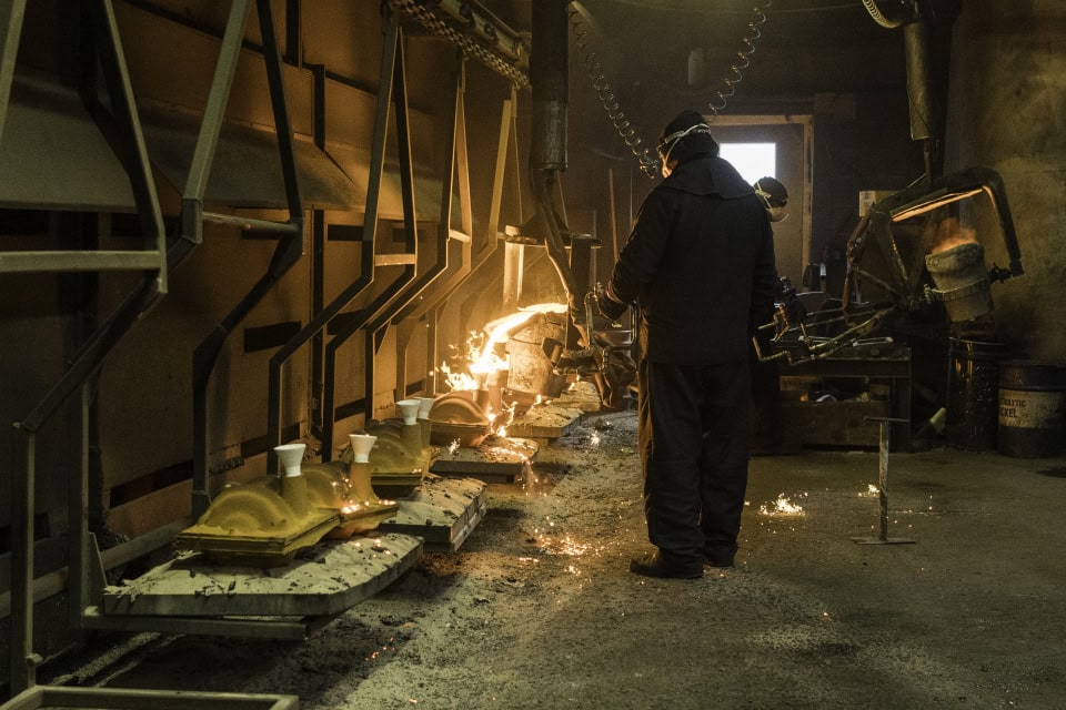 Steelworkers operating in a foundry with molten metal pouring and casting equipment.