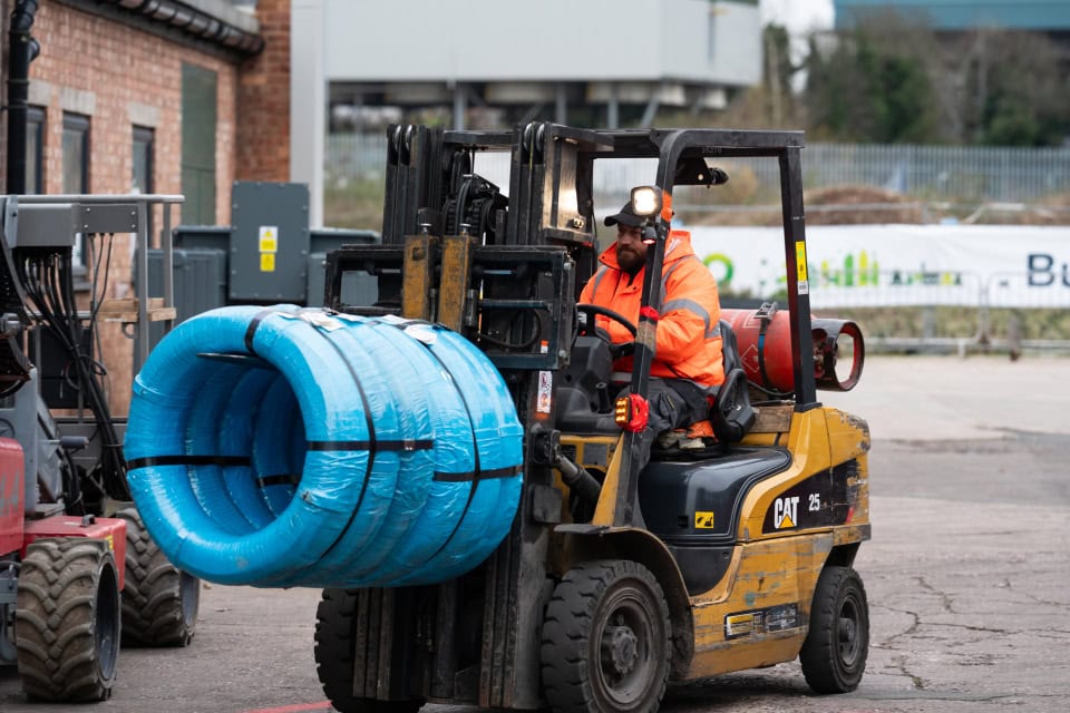 Forklift lifting large blue industrial pipe at construction site.