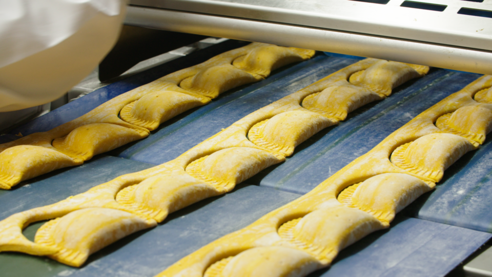 Pastry being shaped on a conveyor belt in a bakery for energy-efficient manufacturing.